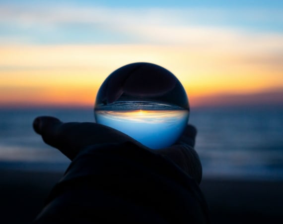 A hand holding a glass ball that's reflecting the sea; there's a sense it's some kind of crystal ball.