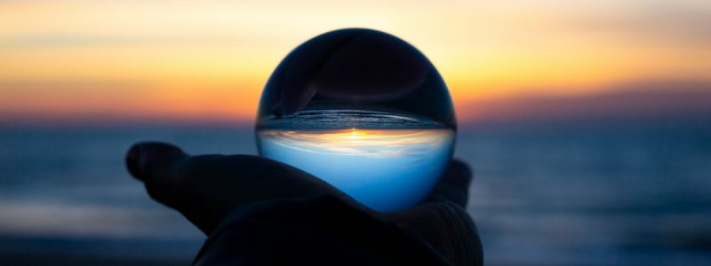 A hand holding a glass ball that's reflecting the sea; there's a sense it's some kind of crystal ball.