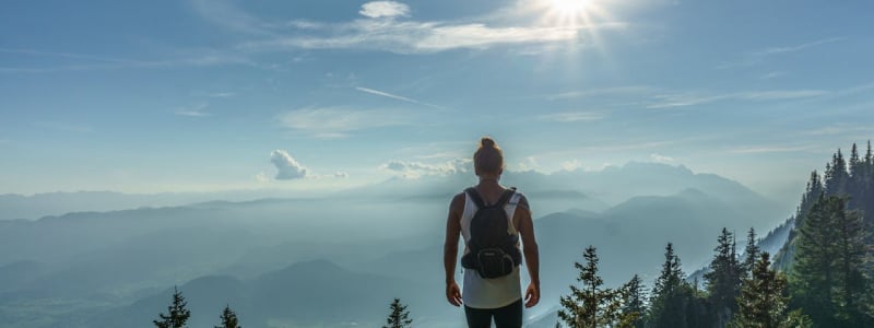 A hiker with a rucksack standing on top of a mountain.