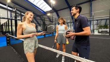 Three people standing on a Padel court holding racquets.