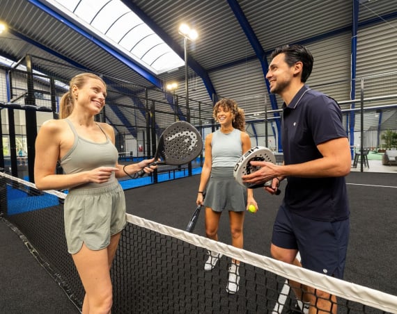 Three people standing on a Padel court holding racquets.