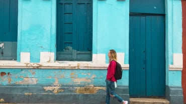 A woman walking past a blue building.