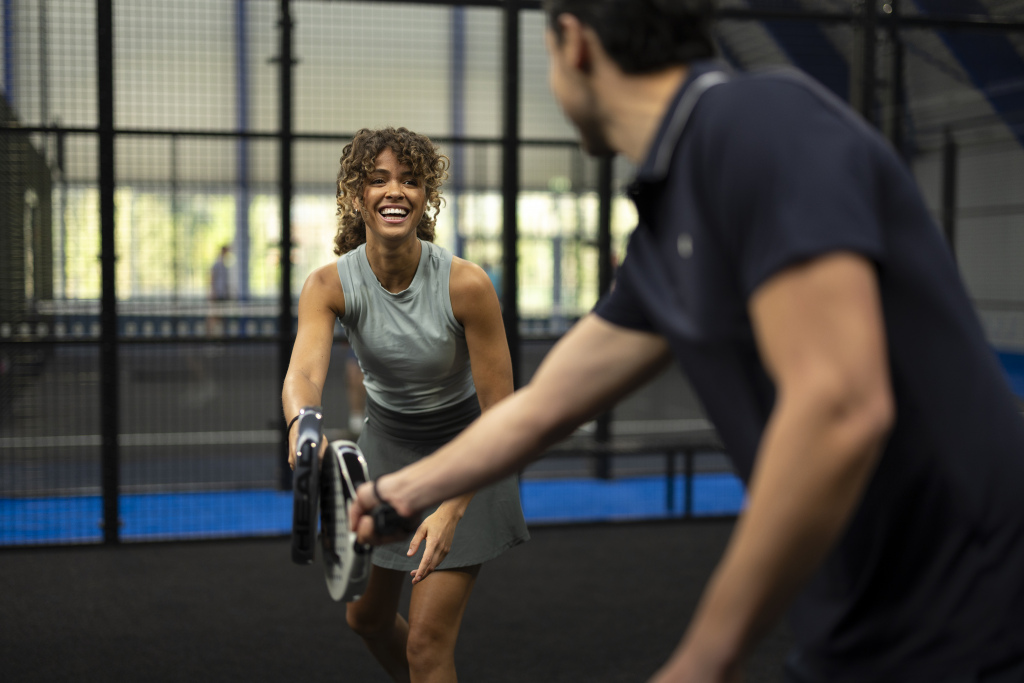 Due persone giocano a padel durante una partita su un campo indoor.