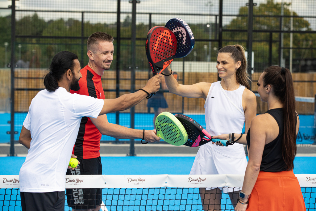 Quattro persone si salutano con le racchette da padel prima di una partita su un campo outdoor.