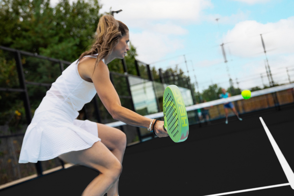 Donna mentre colpisce la palla durante una partita di padel su un campo outdoor.